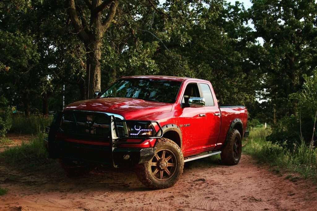 red chevrolet single cab pickup truck parked beside green tree during daytime